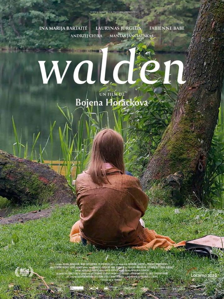 jeune fille assise dans l'herbe de dos, face à un lac.